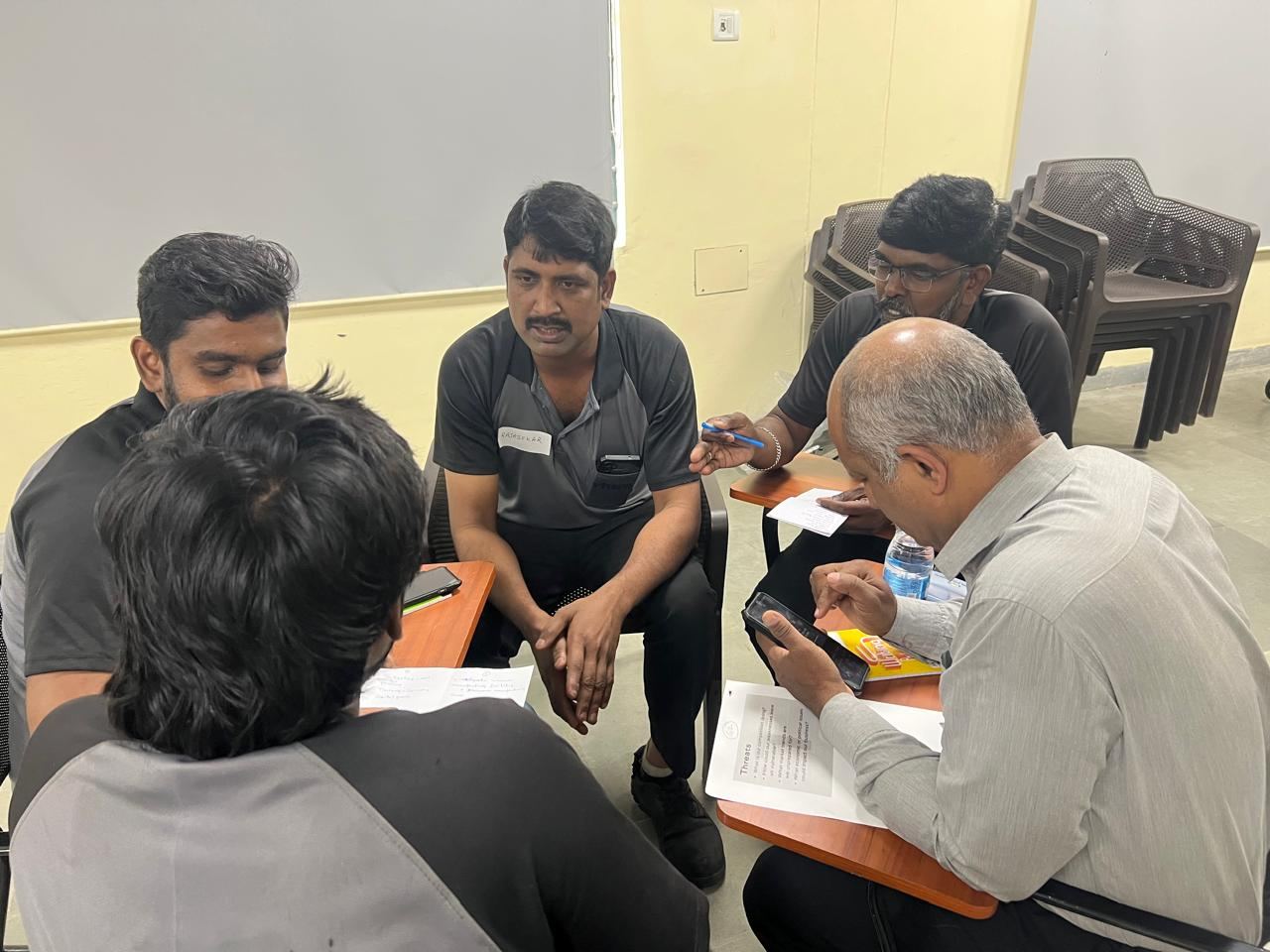 A small group seated in a circle with worksheets, talking through ideas together